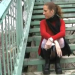 A woman walks around in public looking for a place to poop, and she finally finds a spot by a bridge.